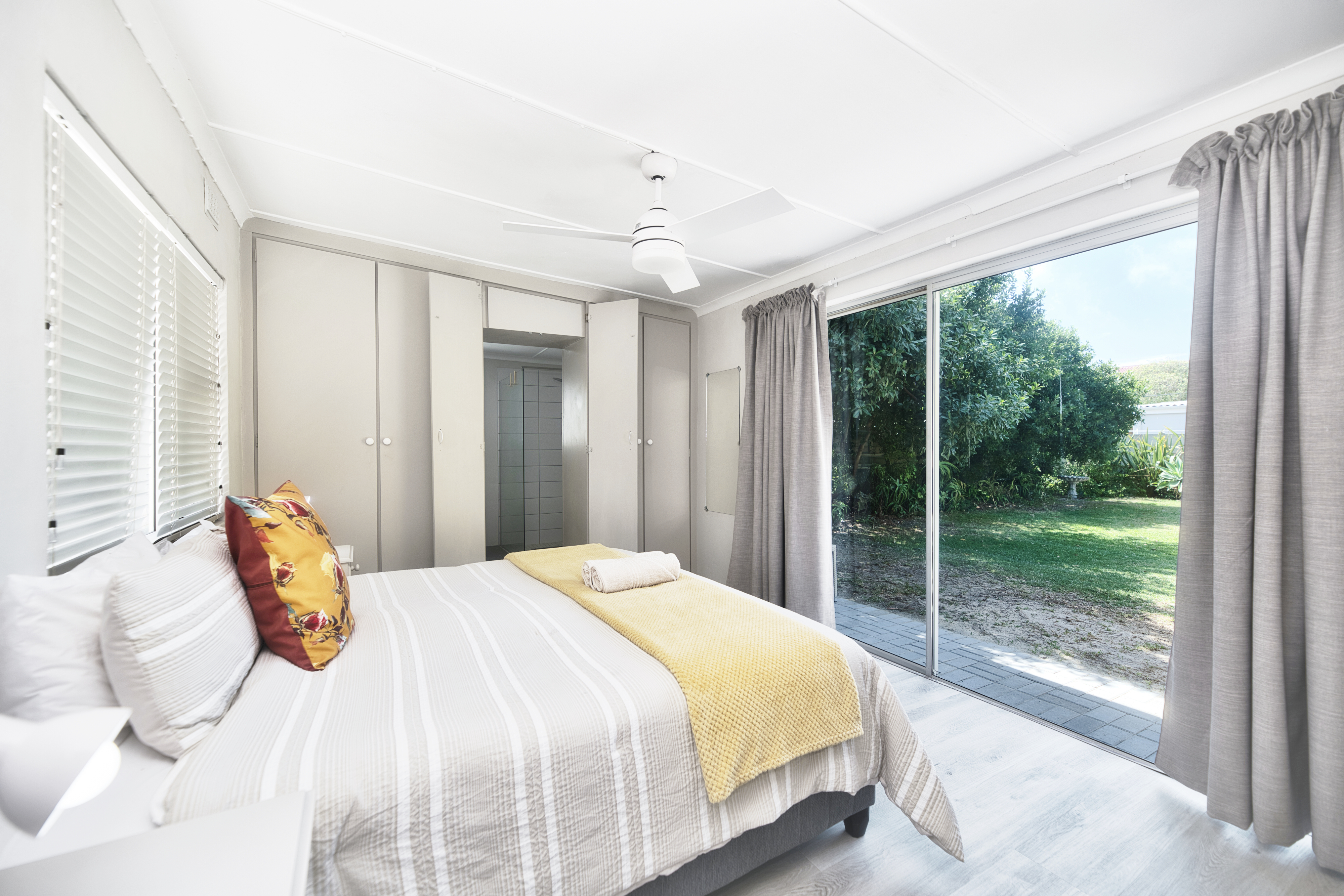 Wake up to sunshine and greenery — a calm, airy bedroom with sliding doors opening onto the garden.